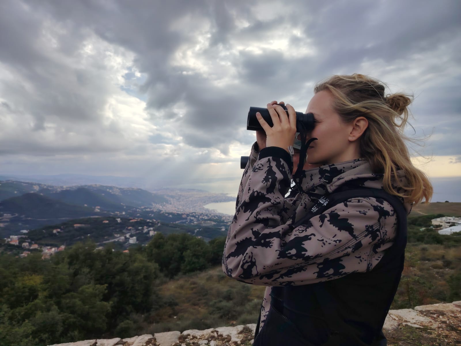 Alexandra using binoculars against a mountainous landscape in Lebanon.