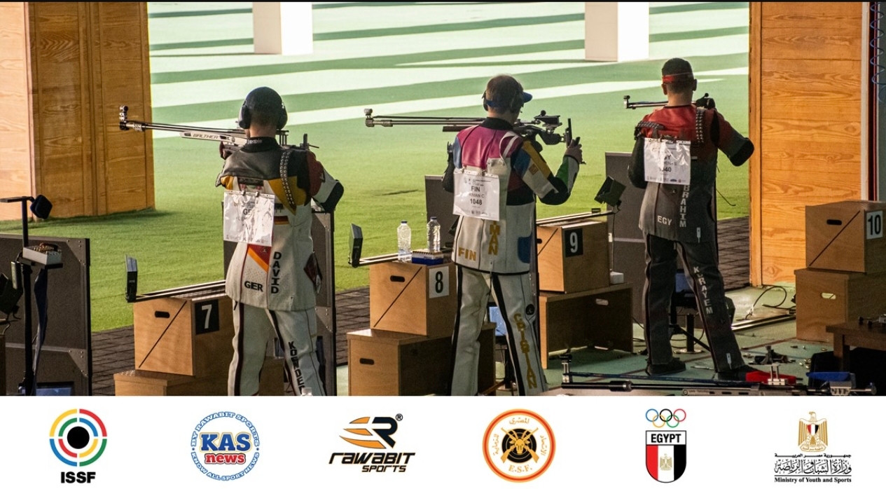 Three rifle shooters take aim from the standing position on a shooting range.
