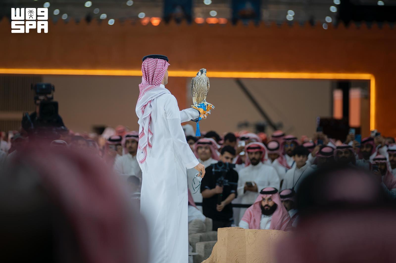 صقّار يحمل صقرًا أمام جمهور المزاد داخل المعرض.